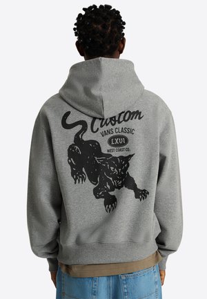 Osoba nosząca szarą bluzę z kapturem z grafiką czarnego pantery i napisem „Custom Vans Classic LXVI West Coast Co.”, widziana od tyłu.
