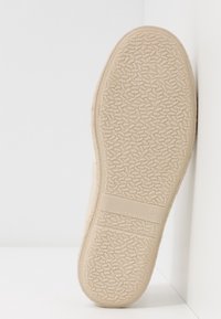 Vaaleanbeige kenkäpohja, jossa on teksturoitu pinta ja pieniä geometrisia kuvioita, merkitty "MADE IN SPAIN" ja koko "37." Suora reuna, hieman kaareva.