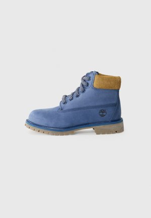 Bottine en cuir bleu avec un col en daim tan, des lacets décoratifs et une semelle robuste, présentant un petit logo sur le côté extérieur.