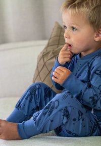 Blå pyjamas i uppsättning med astronaut- och planetmönster, med långa ärmar och manschetter. Mjuk tyg, avslappnad passform och neutral bakgrund.