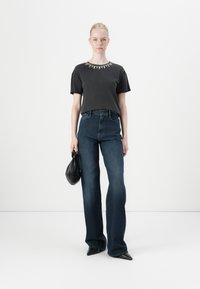 Tricou negru din bumbac cu embellishments metalice la decolteu, asortat cu blugi întuneci din denim cu talie înaltă și o geantă mică neagră.