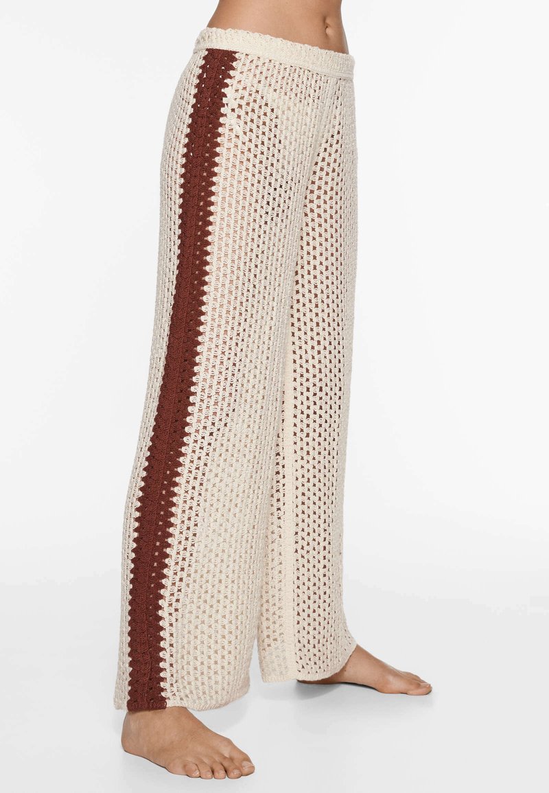 Pantaloni all'uncinetto color crema con una trama aperta e testurizzata. Presentano una striscia laterale bordeaux e una cintura ampia ed elastica. Vestibilità ampia e lunghezza fino al pavimento.