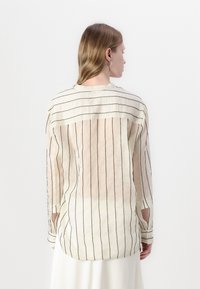Lightweight, sheer shirt featuring vertical black stripes on a cream background, long sleeves, and a rounded hemline.