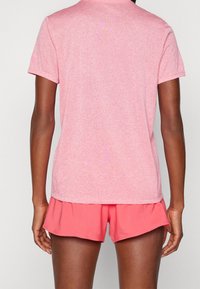 Camiseta corta de manga corta en color rosa jaspeado con un cuello redondo, combinada con pantalones cortos deportivos color coral que cuentan con una cinturilla elástica y un dobladillo en varias capas.