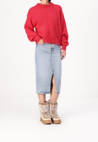 Czerwony dziany sweter o fakturze, niebieska dżinsowa spódnica midi z przednim rozcięciem oraz brązowe botki z futrzaną podszewką i grubą podeszwą.