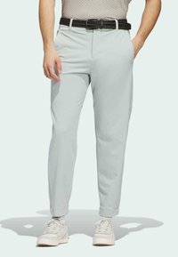 Light green tapered pants with a smooth texture, featuring side pockets, cuffed hems, and a black braided belt. Paired with white sneakers.