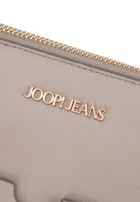 Portafoglio in pelle grigia con hardware dorato. Presenta una texture liscia e il nome del marchio "JOOP! JEANS" in rilievo sulla superficie.