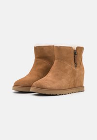 Bottines compensées en daim beige avec fermeture éclair et doublure douce en fourrure au niveau du haut ; semelles en caoutchouc texturé pour une adhérence et une stabilité optimales.