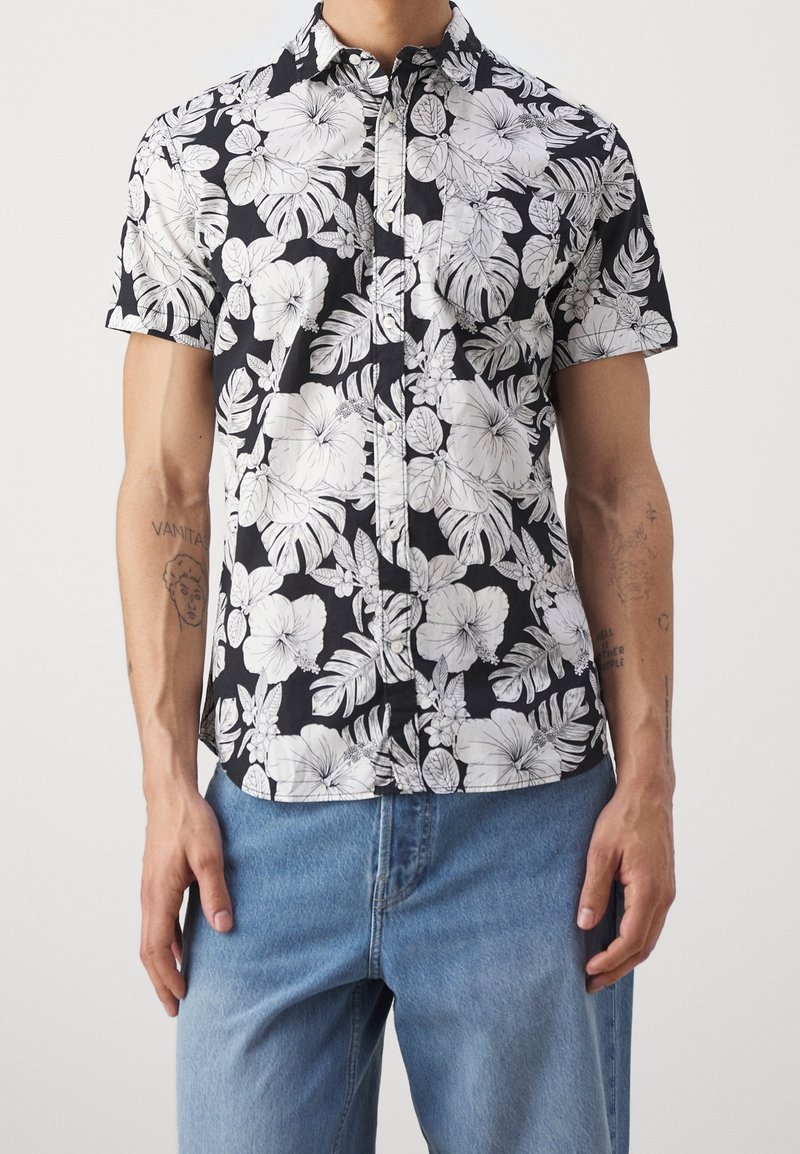 Camicia a maniche corte con bottoni, caratterizzata da uno sfondo nero con motivi floreali e fogliari bianchi, realizzata in tessuto leggero.
