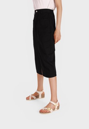 Pantaloni culotte neri alla caviglia con fessure laterali; abbinati a sandali con tacco a cuneo rosa chiaro dotati di cinturini regolabili e una soletta testurizzata.