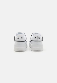 Adidași albi cu un design texturat, accente negre și logo-ul 'AX' pe spate. Talpa groasă oferă înălțime și suport suplimentar.