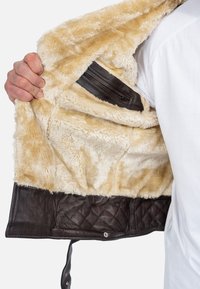 Giacca in pelle marrone foderata con pelliccia sintetica beige, dotata di una tasca interna con zip e dettagli trapuntati lungo l'orlo.