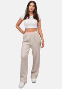 Beige wijde broek met textuurstof en een elastische tailleband, gecombineerd met een aansluitend wit t-shirt met korte mouwen en witte sneakers.