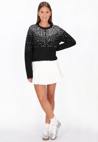 Fekete pulóver, a felső részen flitterekkel, rövid ujjal, fehér plissé szoknyával és ezüst sportcipővel párosítva.