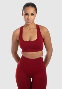 Červený sportovní crop top s širokými ramínky a žebrovanou strukturou, který je spárován s vysokými legínami ve stejném stylu. Hladký, přiléhavý design.