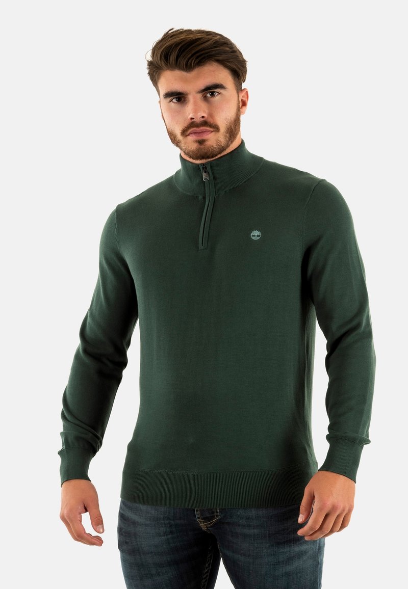 Maglione verde scuro con zip al collo, realizzato in un tessuto liscio ed elasticizzato, con colletto e polsini a coste, dotato di un piccolo logo sul petto.