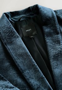 Tmavě modrý sametový blazer s květinovou texturou, klopami a hladkým černým saténovým podšívkou. Viditelná visačka s nápisem "NEXT".