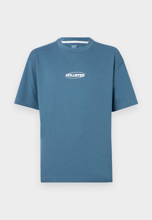 Modra bombažna majica s kratkimi rokavi in okroglo ovratnikom, z belim logotipom "HOLLISTER" na prsih. Gladka tekstura in sproščen kroj.