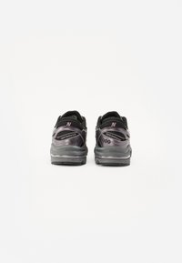 Le sneaker nere New Balance presentano un design elegante con una tomaia testurizzata, dettagli riflettenti e una suola ammortizzata. Numero di modello visibile.