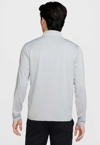 Világosszürke, hosszú ujjú galléros póló, texturált anyagból, egyenes szegéllyel és testhezálló mandzsettákkal.