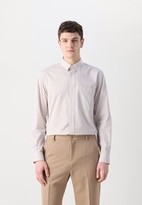 Striped button-up shirt in light beige and cream, featuring a collar and a single chest pocket. Smooth fabric with long sleeves, paired with beige trousers.