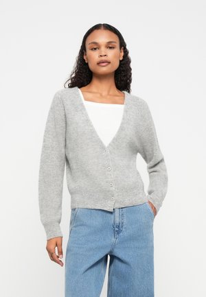 Grauer gestrickter Cardigan mit V-Ausschnitt, langen Ärmeln und einer Fünf-Knopf-Verschluss. Weiche Textur und leicht cropped Passform. Kombiniert mit blauen Jeans.