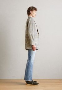 Checkered blazer with a relaxed fit, featuring gray, yellow, and blue stripes. Paired with light wash flared jeans and dark green slip-on shoes.