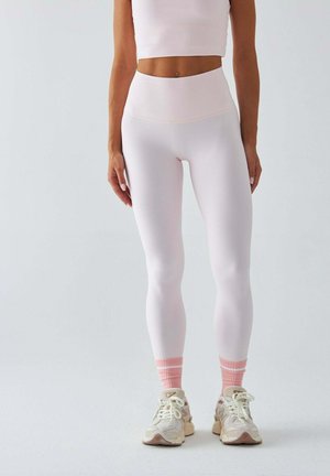 Jasnoróżowy krótki top i pasujące legginsy z wysokim stanem wykonane z gładkiego, elastycznego materiału. Do kompletu białe trampki i skarpetki w różowe paski.