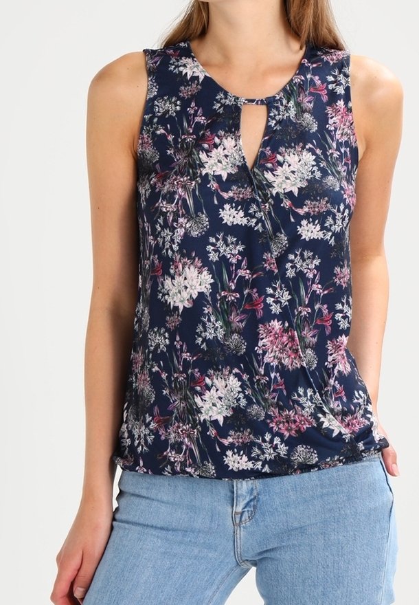 Femme portant un chemisier sans manches bleu marine à motif floral avec un col en goutte d'eau, associé à un jean bleu clair.