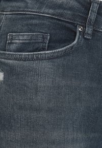 Jeans de mezclilla en azul índigo oscuro con una textura suave, que presentan un bolsillo delantero y ligeros detalles desgastados cerca de la parte superior.