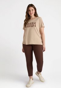 Camiseta de algodón beige con el texto "FRESH" en marrón, combinada con pantalones ajustados marrones y zapatillas ligeras. Diseño simple, de mangas cortas.