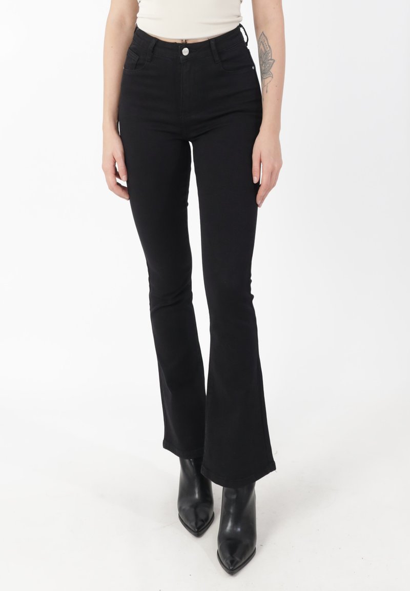 Czarne dzwony z wysokim stanem, z klasycznym designem pięciu kieszeni i jasnymi detalami szwów, w połączeniu z czarnymi spiczastymi butami na obcasie.
