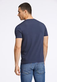 Granatowa, krótko-sleeve koszulka z okrągłym dekoltem. Miękki, gładki materiał. Noszona z niebieskimi dżinsami, podkreślająca dopasowany krój.