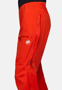 Pantalons imperméables rouges avec des poches latérales zippées et un logo d'éléphant. Ils présentent une texture lisse et une coupe athlétique pour une utilisation active.