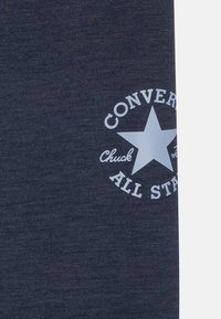 Navyblaues Gewebe mit strukturiertem Finish, das ein kreisförmiges weißes Logo mit einem Stern zeigt, auf dem "CONVERSE CHUCK ALL STARS" steht.