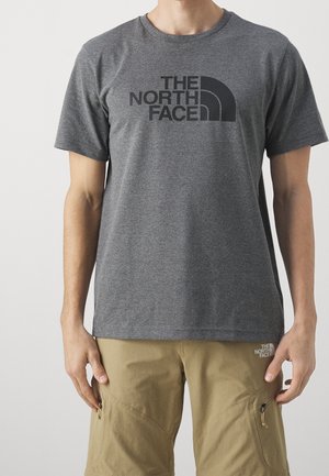 Henkilö, joka käyttää harmaata lyhythihaista t-paitaa ja khakinvärisiä shortseja, molemmissa on "The North Face" -logo.