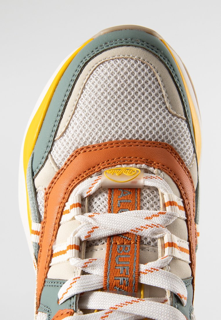 Zapatilla con parte superior de malla y cuero, predominantemente blanca con acentos en verde, naranja y amarillo; cordones planos y cuello acolchado.