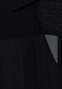 Abito nero in tessuto testurizzato con design a strati. Contiene sezioni contrastanti opache e lucide. Dettagli di cucitura sottili visibili.