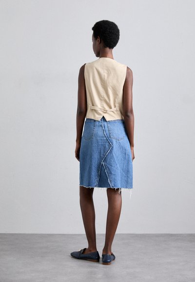 Beige mouwloos topje met een strikdetail aan de achterkant, gecombineerd met een blauwe denim rok met een gebogen naad en een rafelige rand.