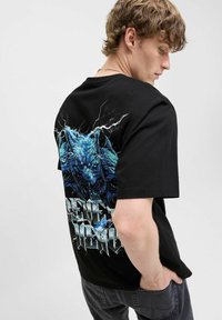 Black cotton t-shirt featuring a blue wolf graphic and lightning design on the back, with bold, jagged text in gray below the image.