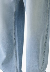 Lähikuva kahdesta jalasta, joissa on vaaleansiniset farkut, joissa on näkyvät sivusaumat ja hienovaraiset varjostusjätkät.