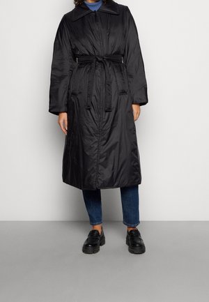 Černý zateplený kabát s límečkem, páskem v pase, dlouhými rukávy a bočními kapsami, nošený přes modré džíny a černé boty.