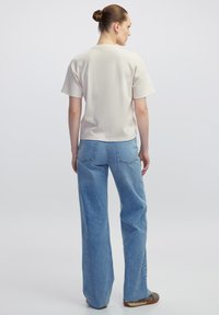 Beżowa bluzka krótki rękaw z okrągłym dekoltem, w połączeniu z wysokimi, jasnoniebieskimi spodniami z szerokimi nogawkami, które mają tylne kieszenie i surowe wykończenia.