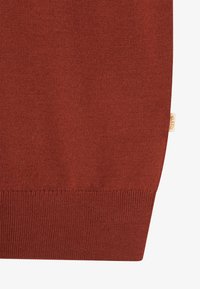 Καστόχρωμο πλεκτό ύφασμα με ριμπ μανσέτα και μια μικρή μπεζ ετικέτα στη δεξιά πλευρά του ρούχου.