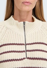 Cremefarbener Strickpullover mit hohem Kragen und einem Reißverschluss vorne, der horizontale weinrote Streifen und eine strukturierte Webart aufweist.