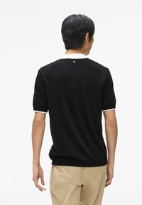 Crna polo majica s bijelim ovratnikom i naglascima na rukavima, izrađena od glatkog materijala. Ima mali logo na stražnjem dijelu ovratnika.