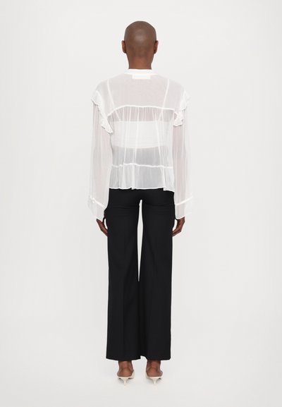 Witte transparante blouse met ruches, lange mouwen en knoopmanchetten, gecombineerd met strakke zwarte pantalon en minimalistische hakken.
