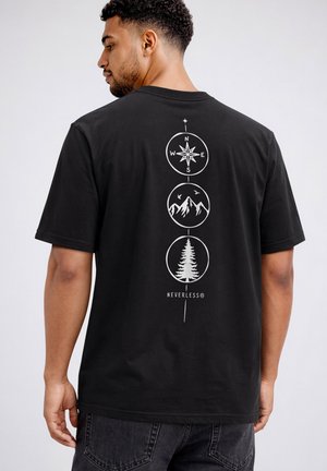Mann trägt schwarzes T-Shirt mit weißen Kompass-, Berg- und Baum-Symbolen, die vertikal auf dem Rücken über dem Wort "NEVERLESS®" angeordnet sind.