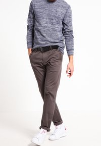Outfit casual con una camicia a maniche lunghe blu navy in tessuto, pantaloni chino marroni e sneakers bianche con dettagli rossi. Cintura in vita.