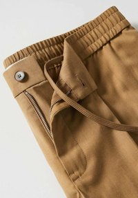Braune Baumwoll-Jogginghosen mit elastischem Bund, Reißverschlusstasche und verstellbarem Kordelzug. Mit einem Knopfverschluss auf der Vorderseite.